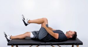 A person performing a knee-to-chest stretch lying on their back on a bench
