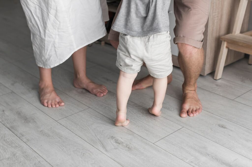 View of parents' feet with little son standing on wooden floor