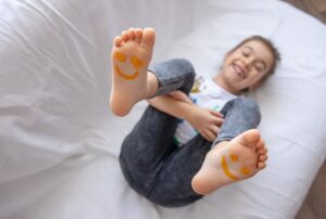 A child with a smiley face painted on her soles is lying on a bed