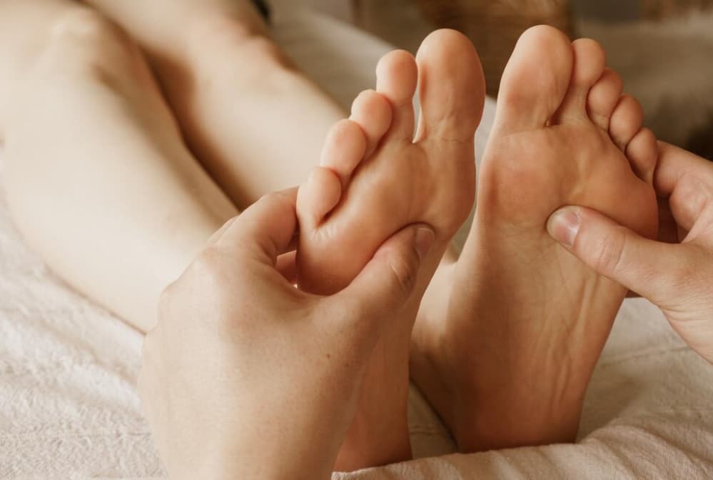 Person massaging the feet of the person on a bed