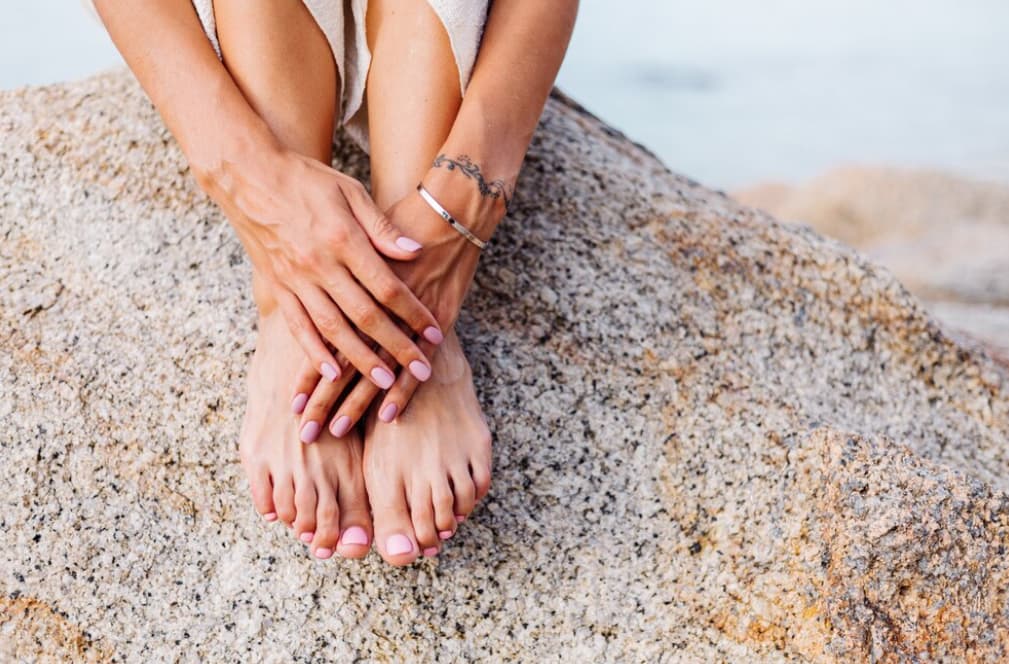 Hands cradling feet on a rocky beach