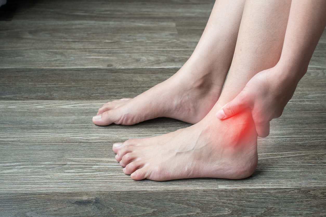 A woman holds her hand on the ankle of a leg with an inflamed joint
