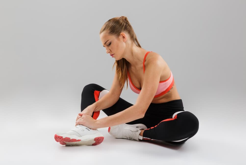 A woman tying her shoe before a workout, on a grey backdrop