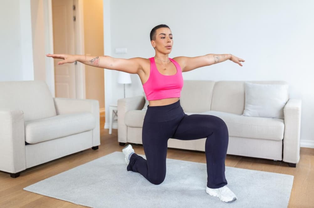 A person in a lunge position with arms extended, indoors